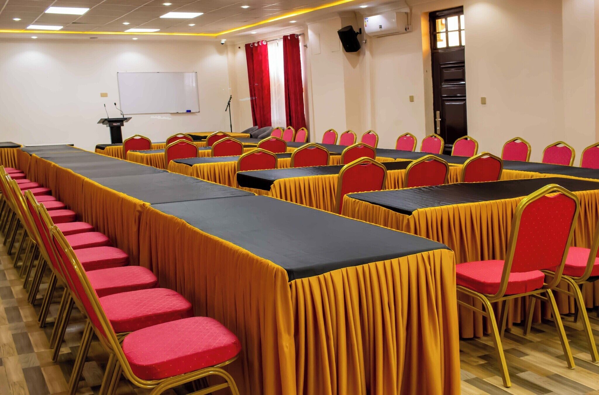 A conference room with rows of tables and chairs, a whiteboard, and a podium.