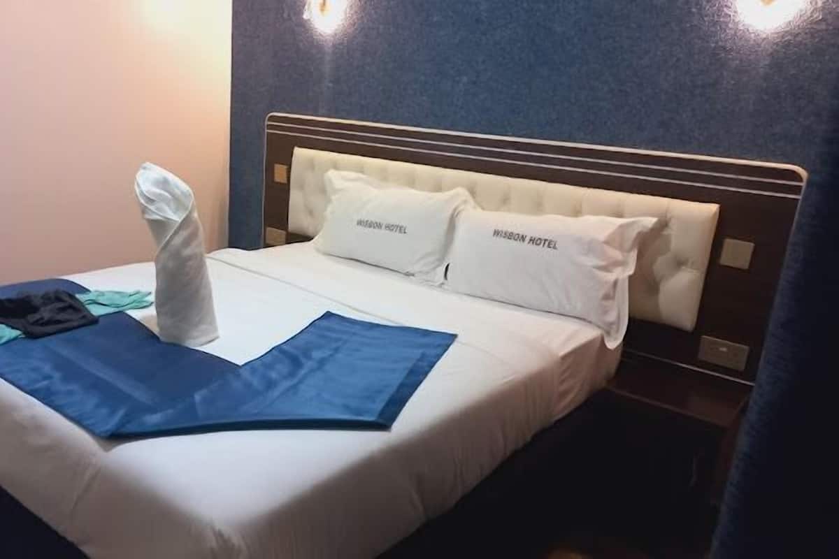 Cama bem arrumada com um cobertor azul, uma toalha dobrada e uma calça ao lado.