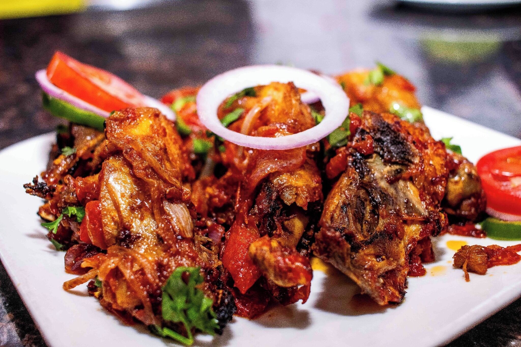 A plate of grilled chicken with vegetables and a slice of tomato.