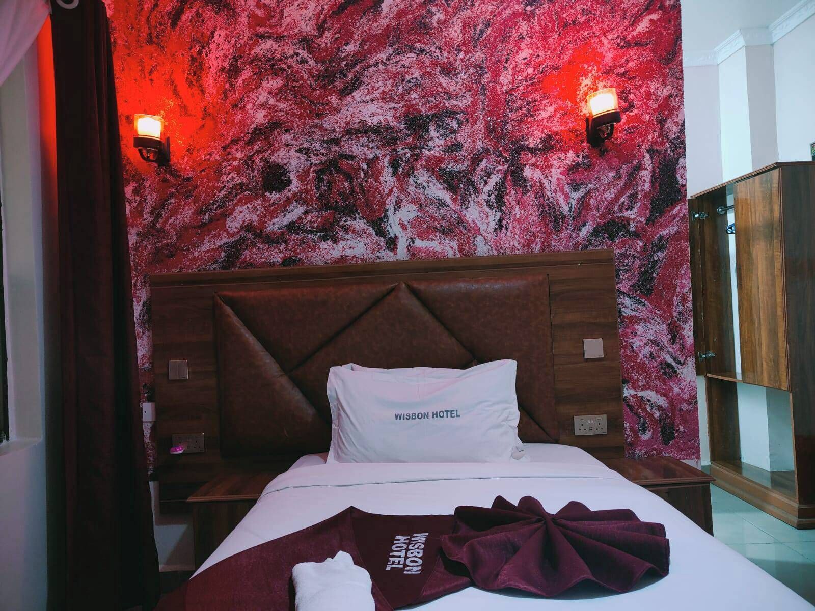 A hotel room with a bed, a headboard, two wall-mounted lights, a nightstand, and a wooden wardrobe.