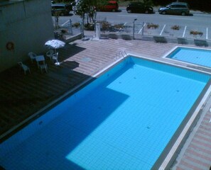 A swimming pool with a tiled deck, a few lounge chairs, and a small garden area with plants. - Beautifully Renovated Flat With Shared Pool (Rosolina)