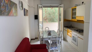 A compact kitchen with a dining area, a red sofa, and a view of trees through the open door. - Beautifully Renovated Flat With Shared Pool (Rosolina)