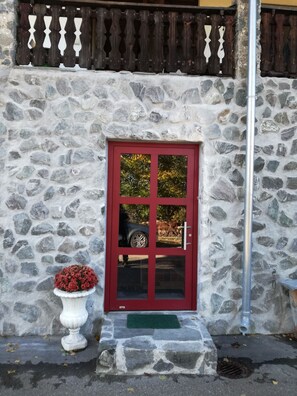 A stone building with a red door, a white flower pot, and a metal pipe. - Nature Céleste 2 - 2-room ground-floor apartment in Black Forest style between Titisee and Schluchsee (Feldberg (Schwarzwald))