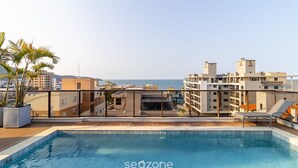 Ein Pool auf dem Dach mit Blick auf Stadt und Meer, umgeben von Gebäuden.