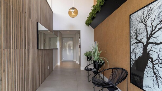 Ein modernes Interieur mit einer Holzwand, einem schwarzen Stuhl, einer Topfpflanze und einem gerahmten Baum-Kunstwerk.