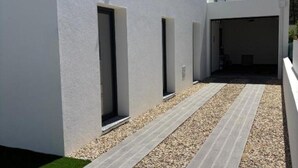 A modern building with a clean, white exterior, a gravel pathway, and a series of doorways leading to interior spaces. - Holiday home with pool 15 minutes walk from the beach and 5 minutes from Aroeira golf course (Almada)