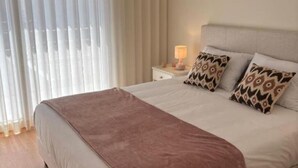 A neatly made bed with a brown blanket, two patterned pillows, and a bedside lamp on a white nightstand. - Holiday home with pool 15 minutes walk from the beach and 5 minutes from Aroeira golf course (Almada)