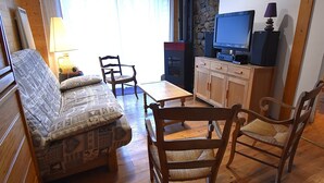 Una sala de estar con sofá, dos sillones, una mesa de centro, televisor y una pared de piedra.