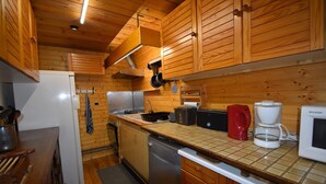 Una cocina compacta con armarios de madera, un lavamanos de acero inoxidable, un lavavajillas y una cafetera.