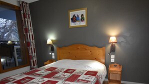 Een slaapkamer met een houten hoofdbord, een gewatteerde spreideken, twee bedlampen, een ingelijste foto aan de muur en een raam met gordijnen.