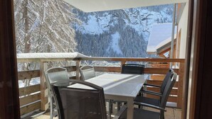 Een balkon met een tafel en stoelen, met uitzicht op een besneeerd berglandschap.