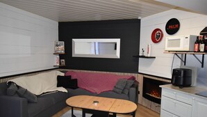 A compact living space with a sofa, a small table, a fireplace, a microwave, and a shelf with bottles.