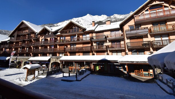 A multi-story hotel with balconies, a ski slope in the background, and a clear blue sky.