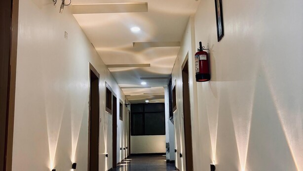 A long, narrow hallway with a polished floor, recessed lighting, and a fire extinguisher mounted on the wall. - Hotel Ambrosia Delhi Airport (New Delhi)
