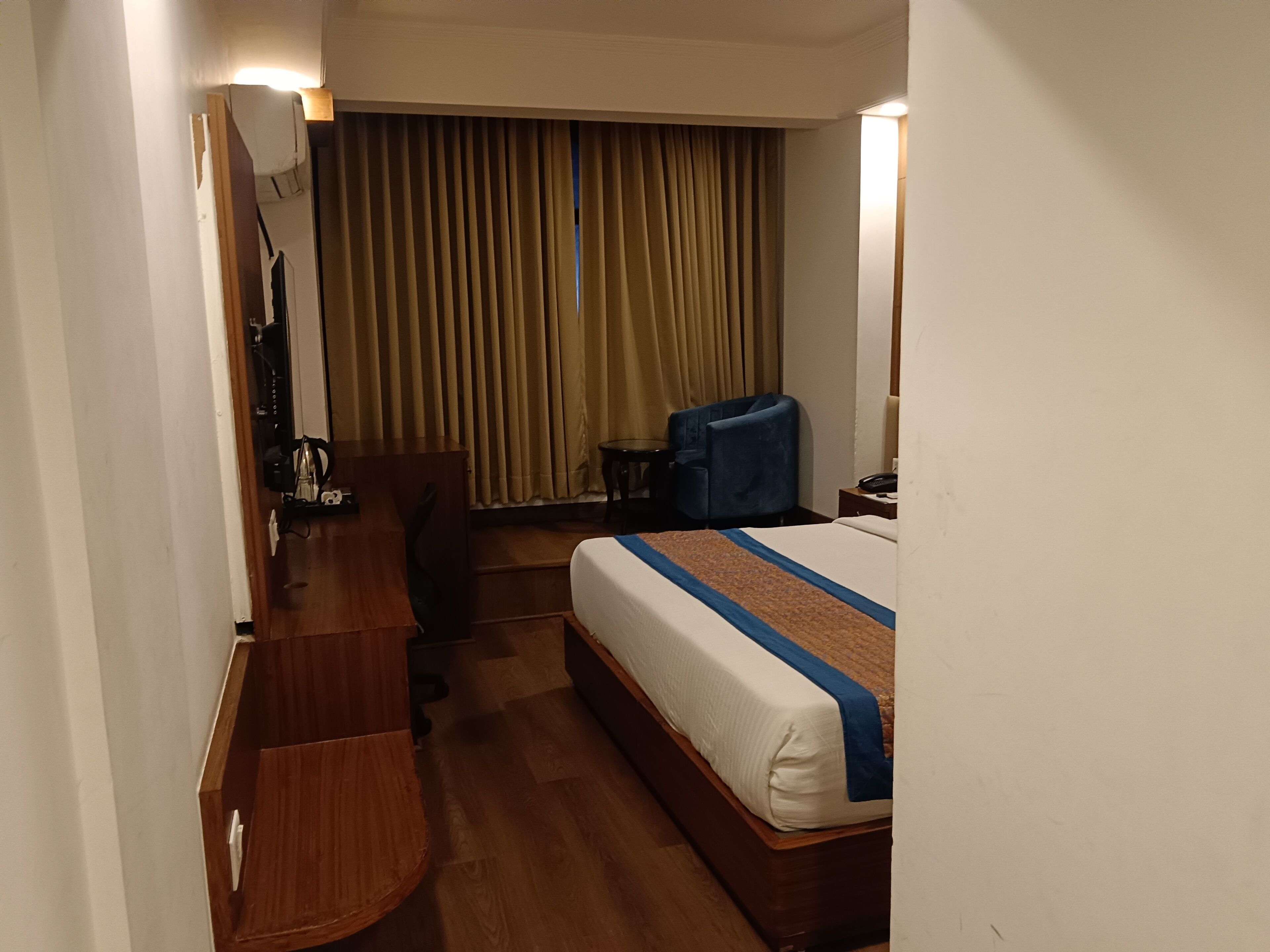 A hotel room with a bed, a desk, a chair, a lamp, and a curtain.