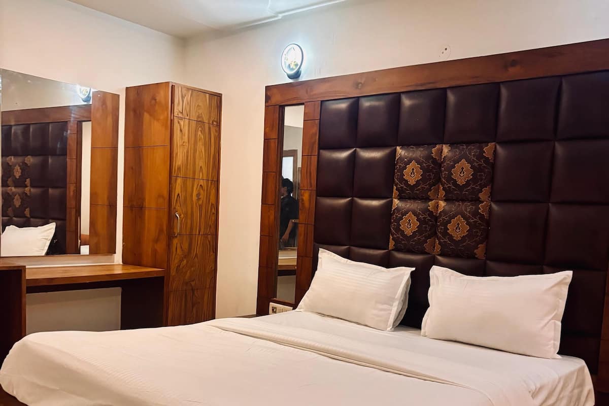 A bedroom with a large bed, wooden wardrobe, and a mirror.