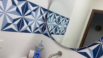 Ein Badezimmer mit geometrisch gemusterten Fliesen an der Rückwand, einem Spiegel, einem Waschbecken und einer Seifenspender.