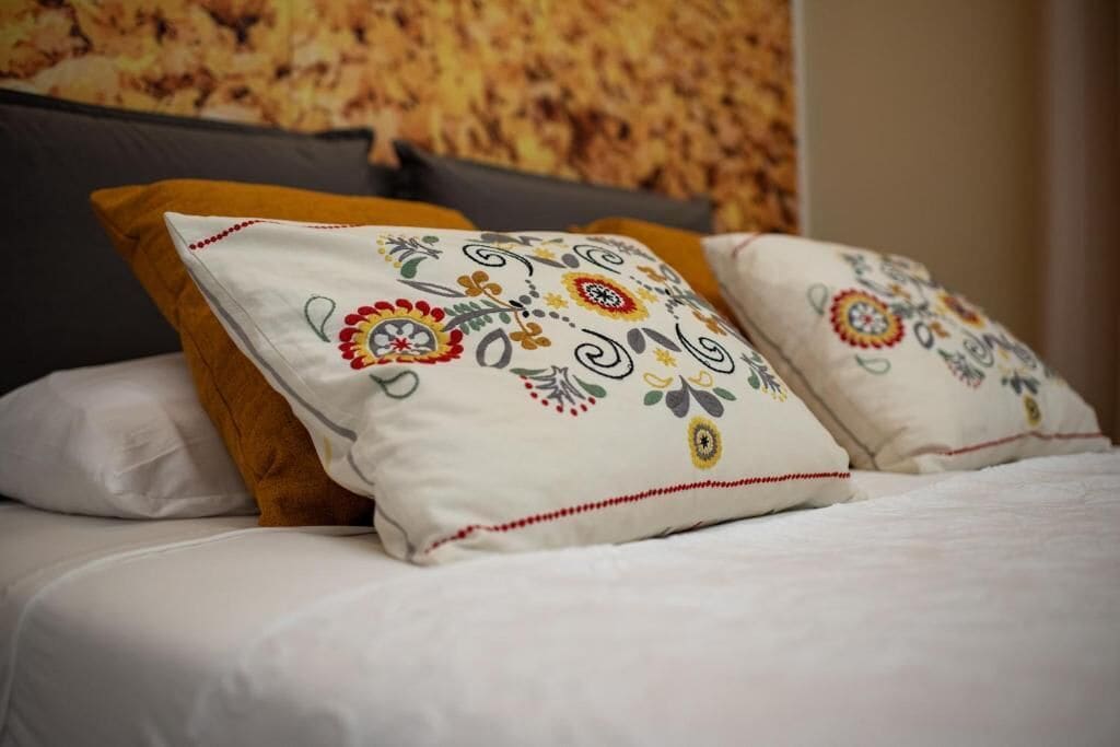 A bed with white bedding and decorative pillows with floral patterns.