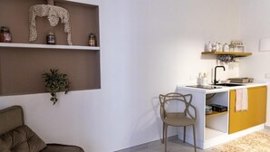 A compact living space with a kitchenette, a sofa, a chair, and shelves with jars and a plant. - San Nicolicchio (Taranto)
