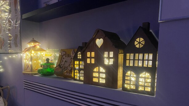 A shelf with various illuminated decorative items including a lantern, a clock, and houses with windows. - San Nicolicchio (Taranto)