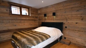 A wooden-paneled room with a bed, a window, and two wall-mounted lamps. - Flocon 2 - One Bedroom Apartment, Sleeps 4 (Vaujany)