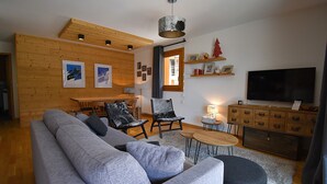 Una sala moderna con un sofá gris, dos sillones, una mesa de comedor de madera y un televisor.