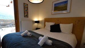 Una cama impecable con almohadas blancas y negras, un cabecero de madera y un cuadro con un paisaje colgado encima.