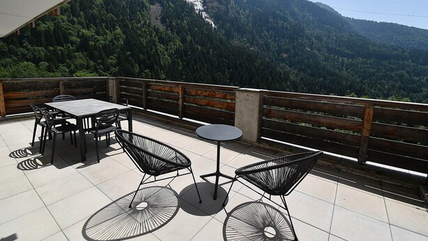 Una terraza con una mesa y sillas, con vistas a un paisaje montañoso que incluye una cascada.