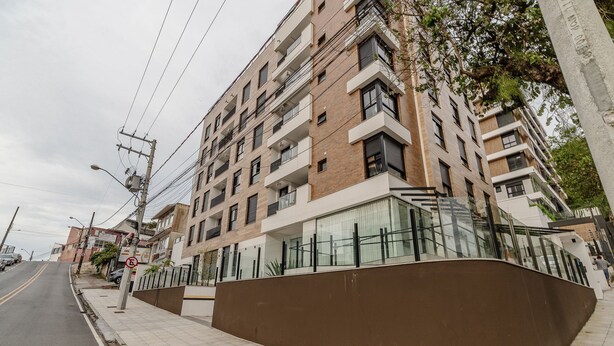 Un edificio residencial de varios pisos con balcones, una acera y una calle.