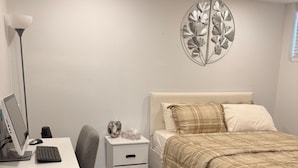 Ett sovrum med en säng, ett skrivbord med en dator, en lampa och en dekorativ väggdekoration.