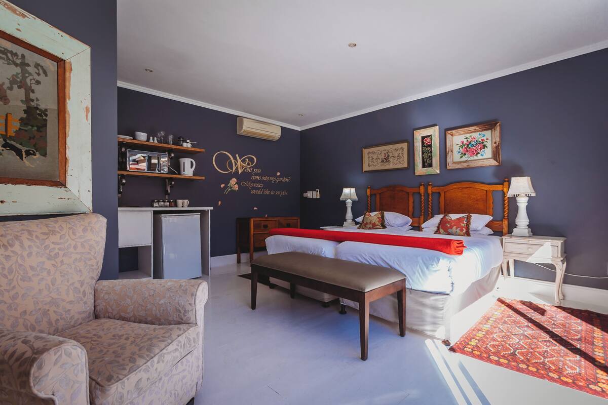 A bedroom with a bed, bedside tables, a bench, a dresser, and a small kitchenette.