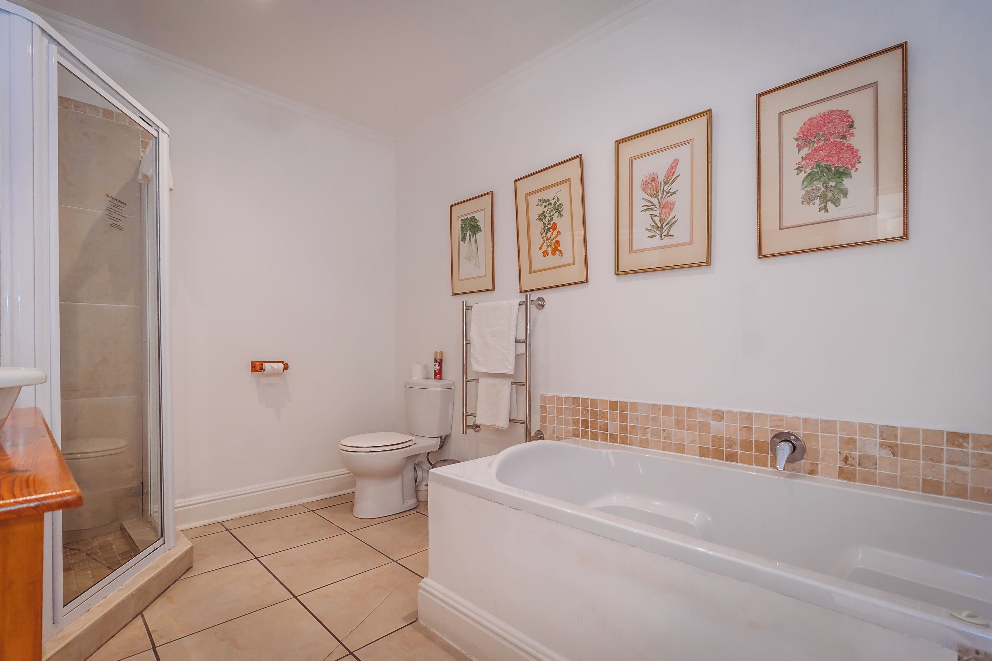 Un baño con bañera, inodoro y ducha. Hay impresiones botánicas enmarcadas en la pared.