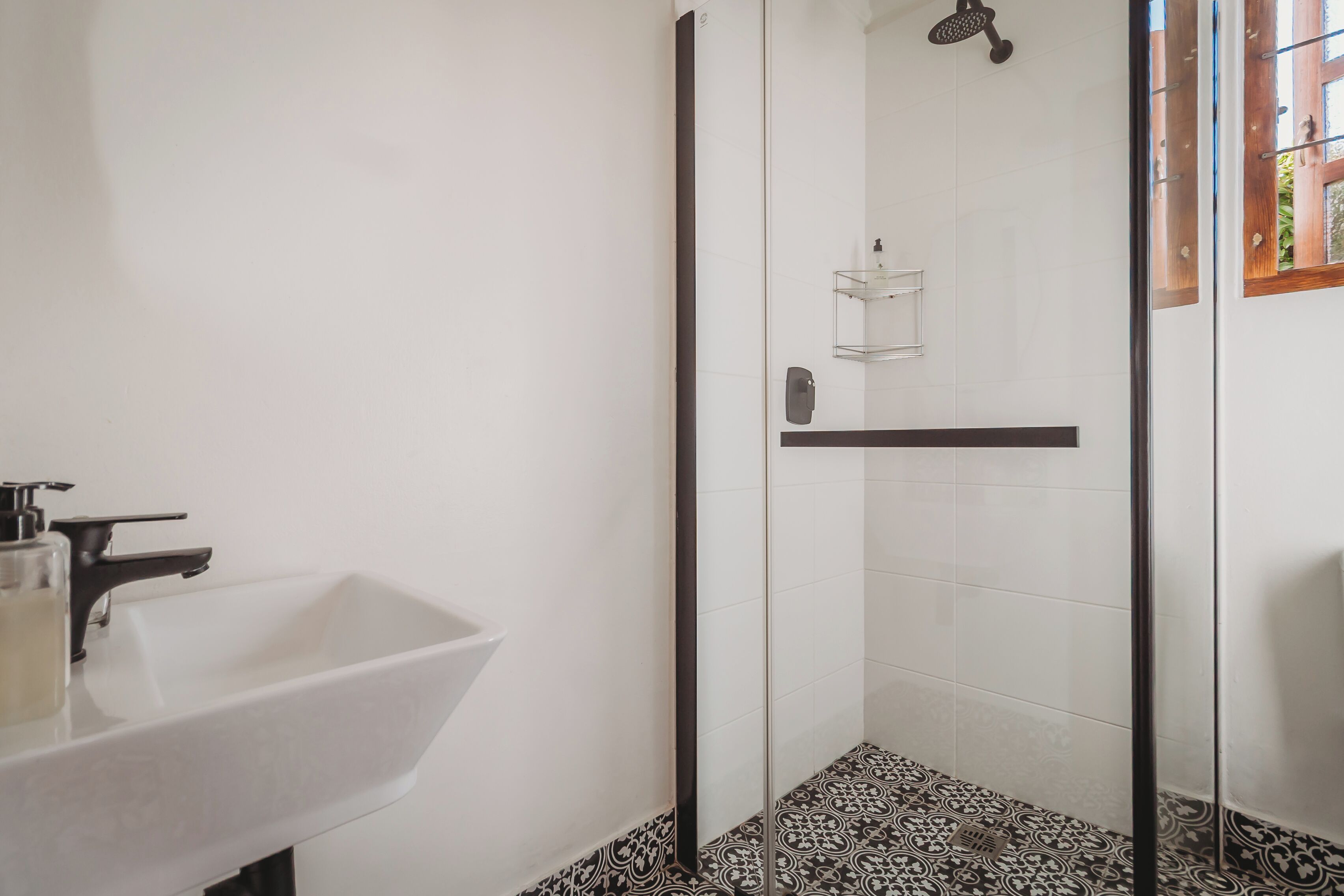 Une salle de bain avec un lavabo blanc, une cabine de douche en verre et des carreaux de sol à motifs.