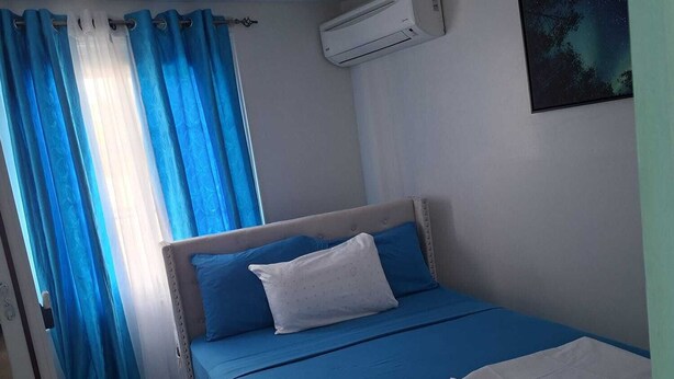 A bedroom with a bed, curtains, an air conditioner, and a wall-mounted picture.