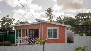 A small, single-story house with a red exterior and white trim, a balcony with a lattice railing, and a white picket fence.