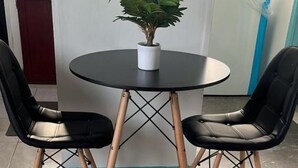 A round table with two black chairs, a potted plant, and a white vase.