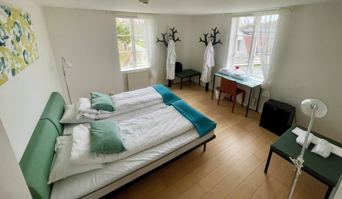 A bedroom with a bed, a desk, and a chair. There are two coat hooks on the wall.