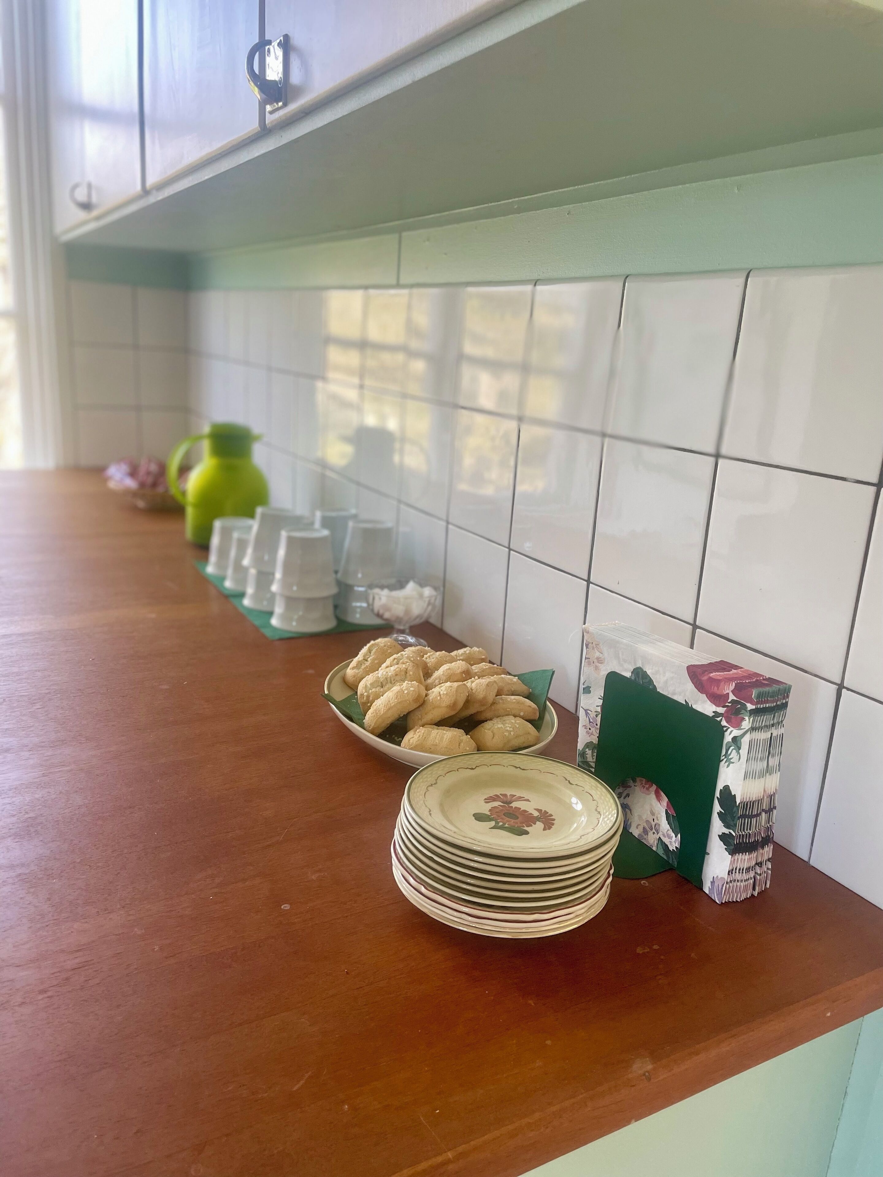 A kitchen counter with a stack of plates, a bowl of cookies, and a green pitcher.