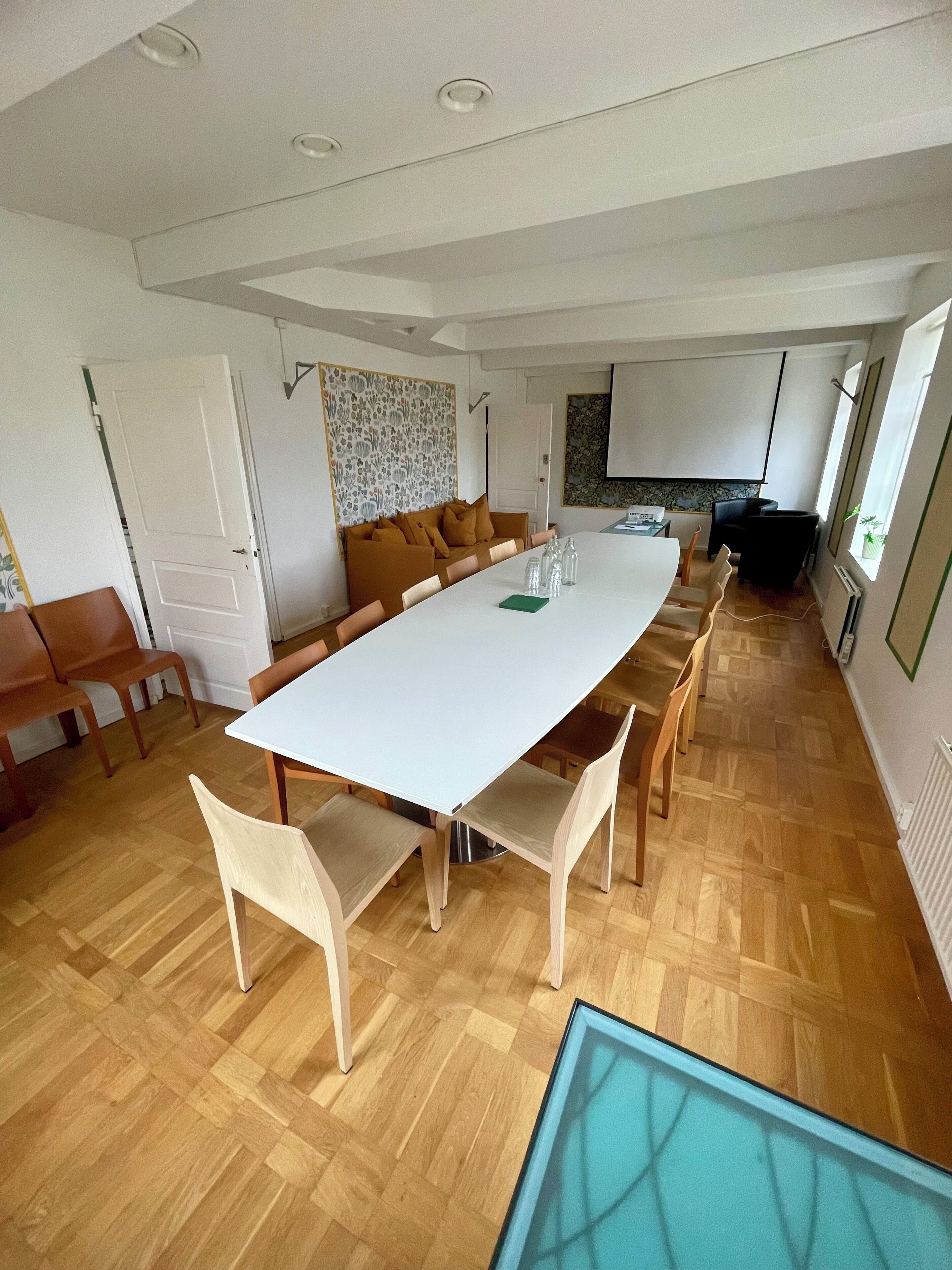 A spacious dining area with a long white table, wooden chairs, and a brown sofa.