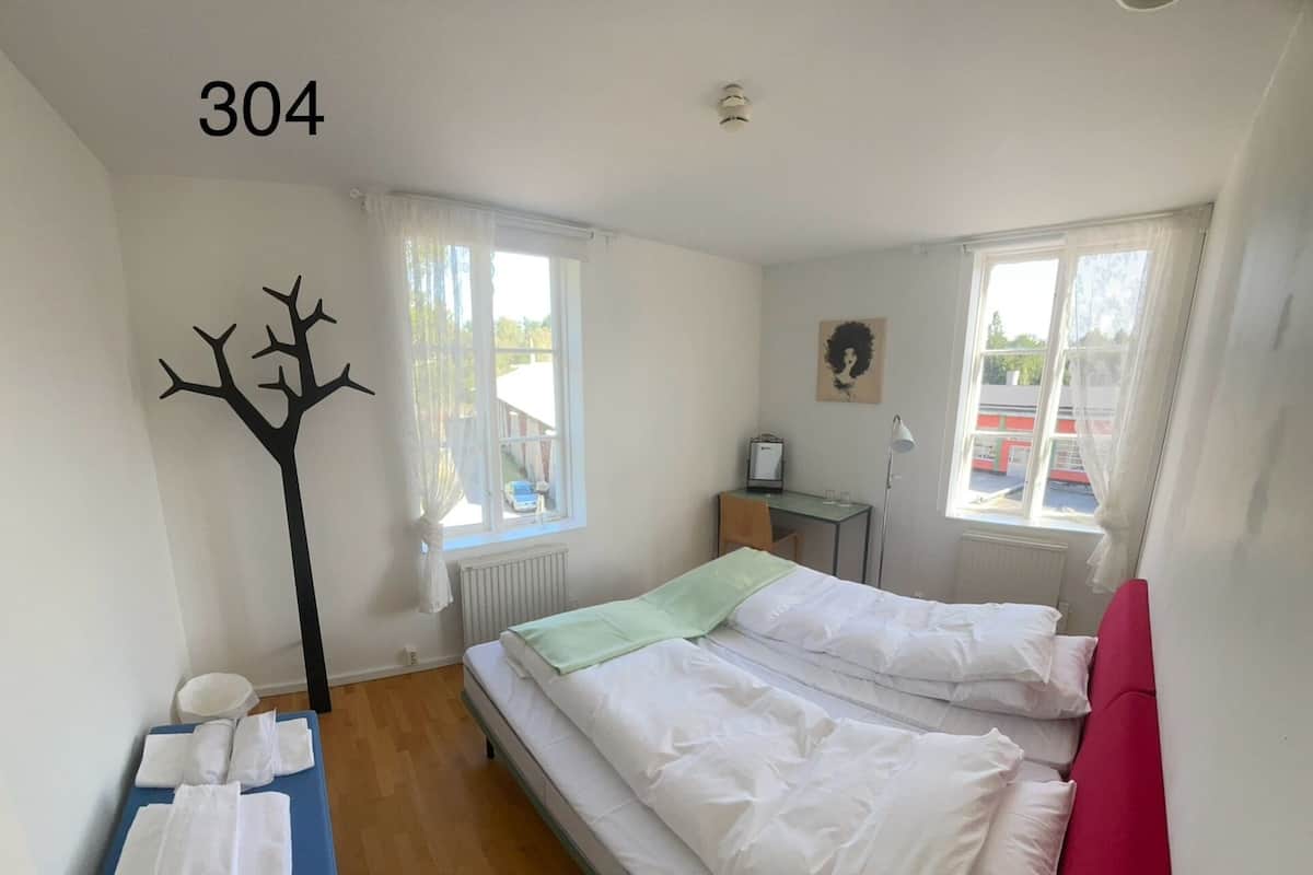 A bedroom with a bed, a table with towels, a coat rack, and a window.