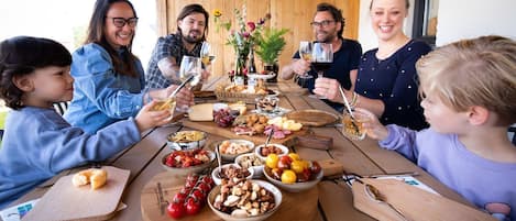 A group of people seated around a wooden table with various food items and drinks, suggesting a casual dining or social gathering.