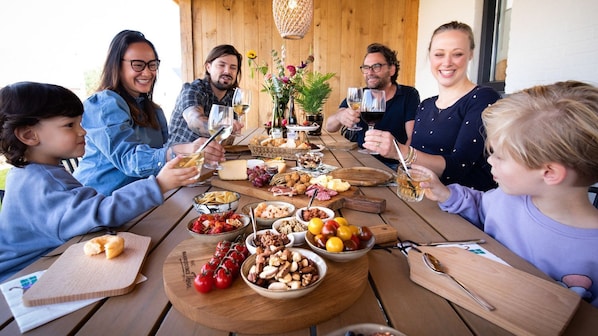 A group of people seated around a wooden table with various food items and drinks, suggesting a casual dining or social gathering.