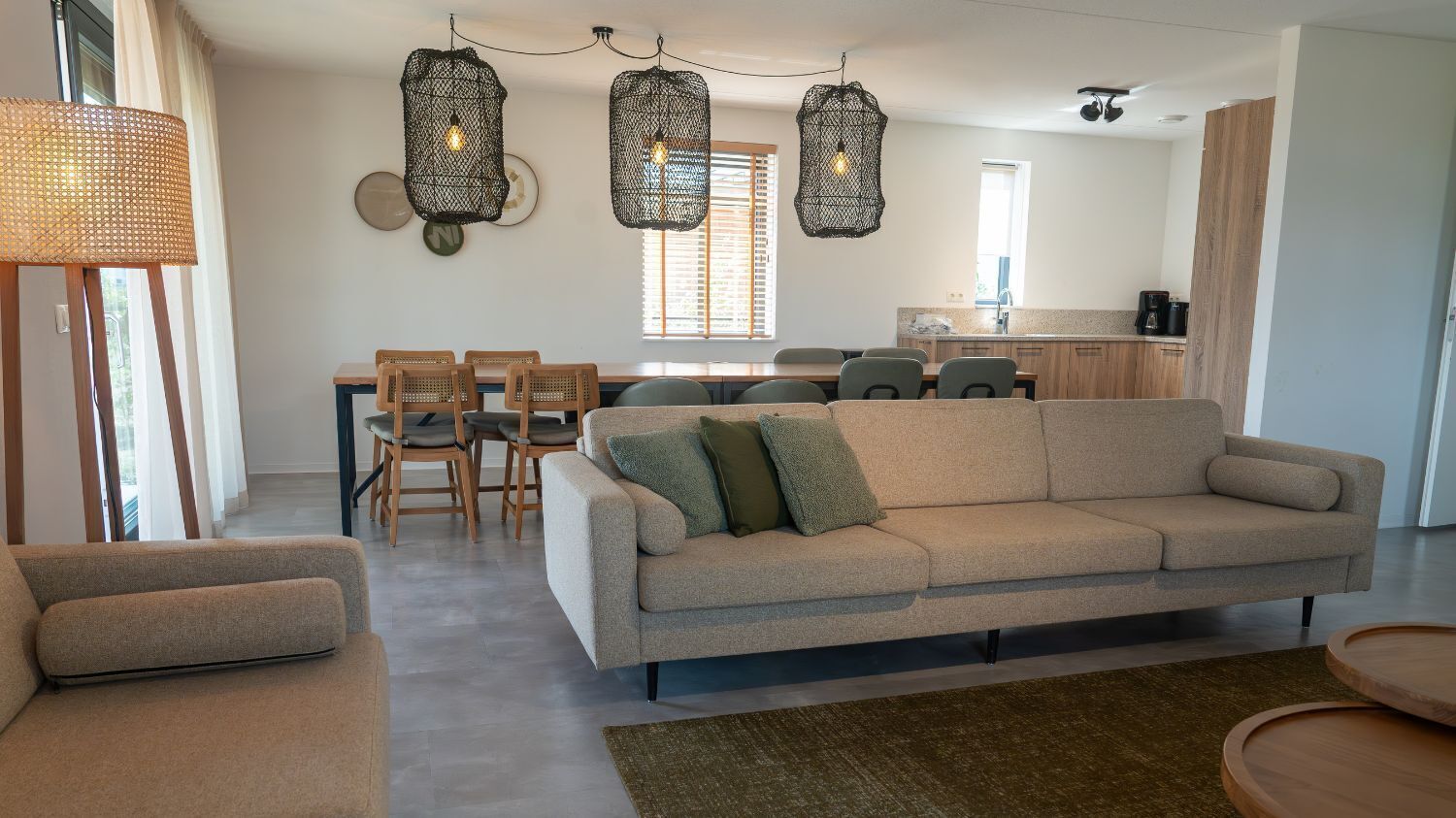 Un salon moderne avec un canapé, des fauteuils, une table à manger et un coin cuisine à l’arrière-plan.