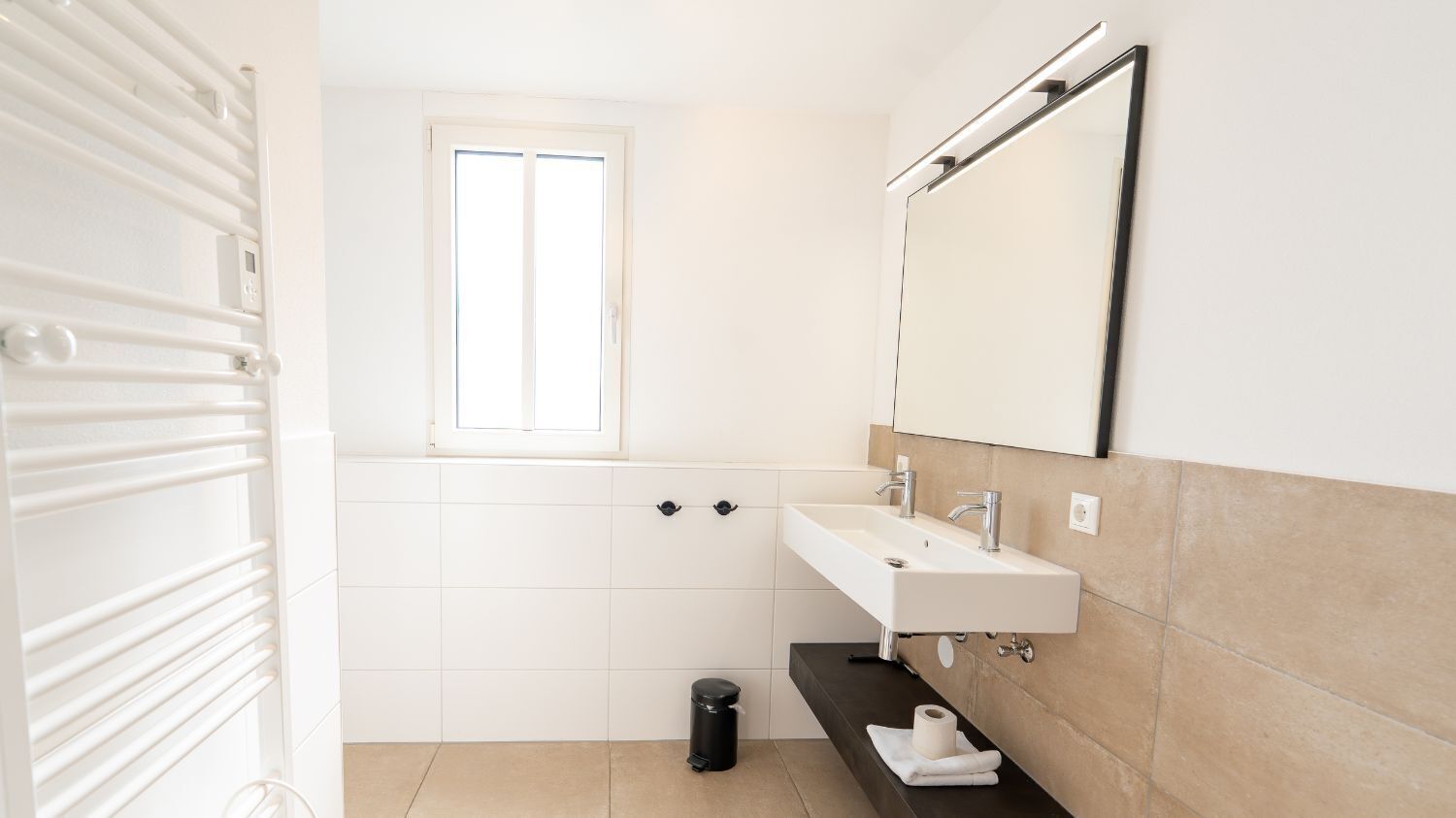 A modern bathroom with a white vanity, a mirror, and a window.