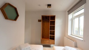 Een kamer met een ingebouwde houten garderobe, een kapstok en een groot raam dat voor natuurlijk licht zorgt.