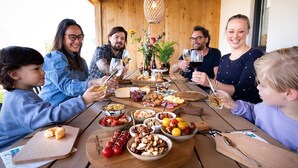 Une famille est assise autour d’une table en bois, et différents plats et boissons y sont servis.