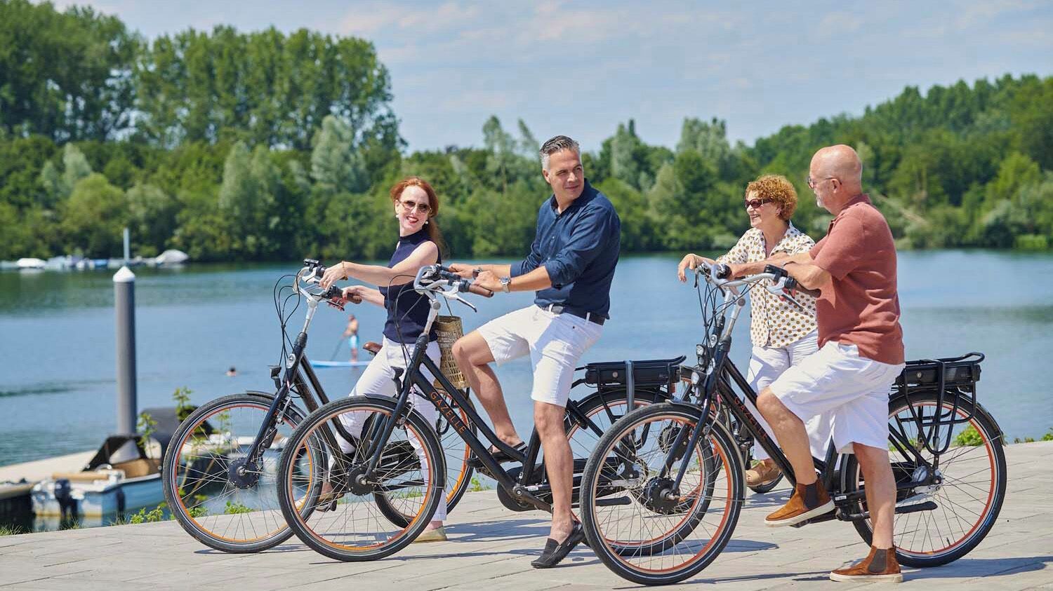 A group of people riding bicycles on a paved path by a lake.
