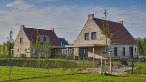 Une maison moderne à deux étages, dotée d’une façade en pierre et d’un toit recouvert de tuiles rouges, entourée d’une pelouse bien entretenue et d’un petit jardin.