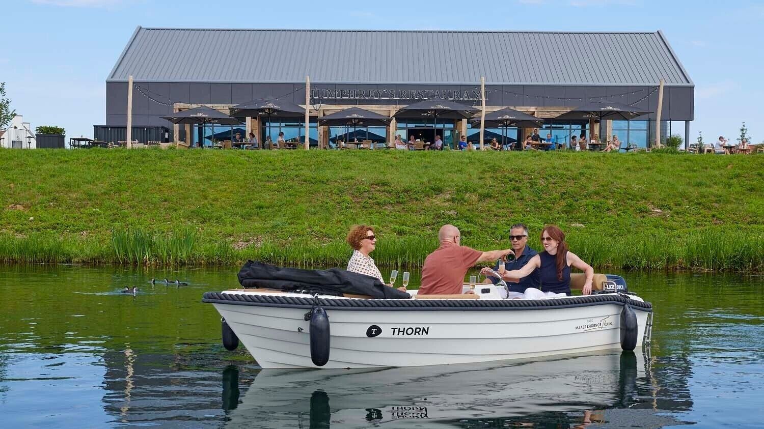 Ein Boot mit Personen in der Nähe eines Gebäudes mit Außenbestuhlung.