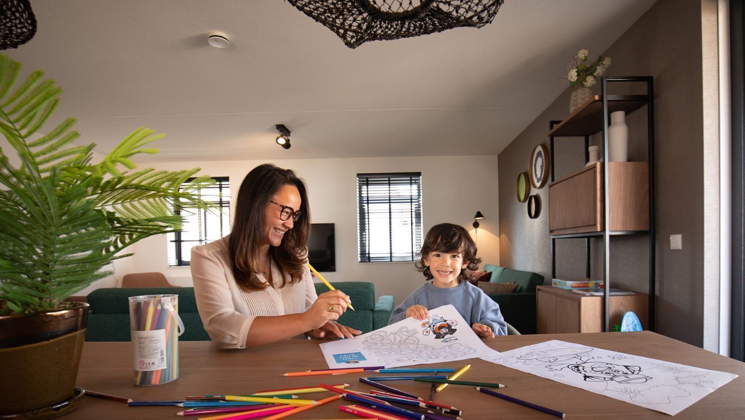 Un salon avec une table en bois, une plante en pot et un enfant qui colorie.